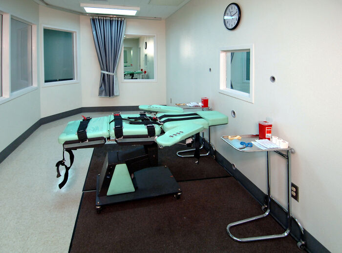 Medieval t*****e device resembling a strapped restraint table in a stark room with medical supplies nearby.